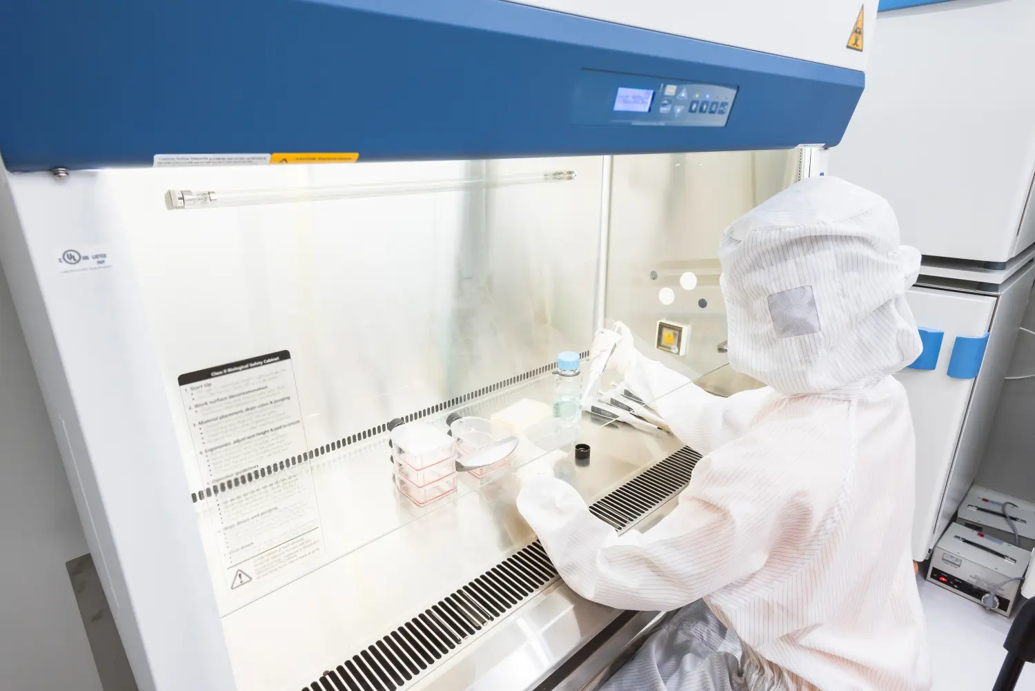 Ein Wissenschaftler im sterilen Overall pipettiert Medium oder Reagenzien für Zellkulturexperimente in einer biologischen Sicherheitswerkbank. Biologische Forschung in sauberer Umgebung. Reinraumanlage